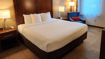 A hotel room with a large bed, two bedside tables with lamps, a chair, and a window with curtains.