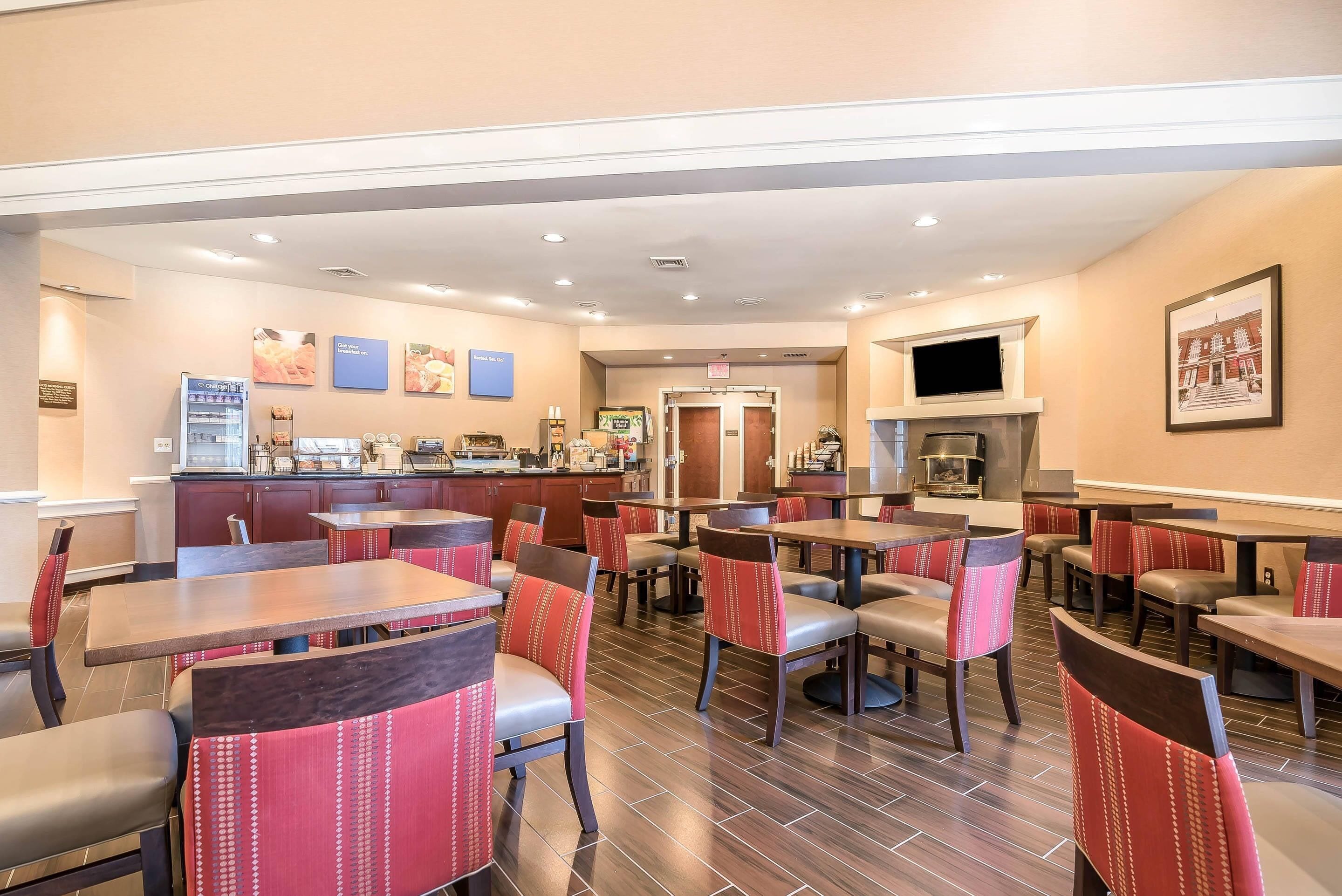 A restaurant with multiple tables and chairs, a counter with a beverage dispenser, and a television mounted on the wall.