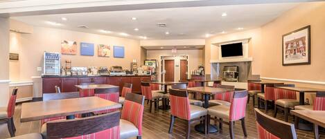 A restaurant with multiple tables and chairs, a counter with a beverage dispenser, and a television mounted on the wall.