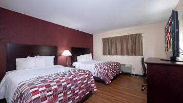 A hotel room with two beds, a desk, a television, and a window with curtains.