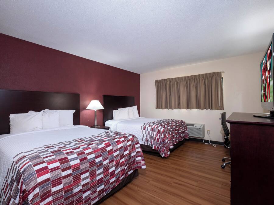 A hotel room with two beds, a desk, a television, and a window with curtains.