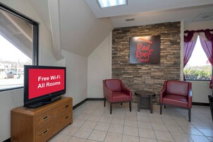 Habitación de Red Roof Inn con televisor mostrando 'Wi-Fi gratuito en todas las habitaciones', dos sillones de cuero, una mesita pequeña y una pared de piedra.