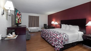 A hotel room with a bed, bedside tables, a desk, a television, and a lamp.