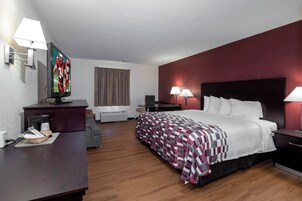Una habitación de hotel con cama, mesitas de noche, escritorio, televisor y lámpara.