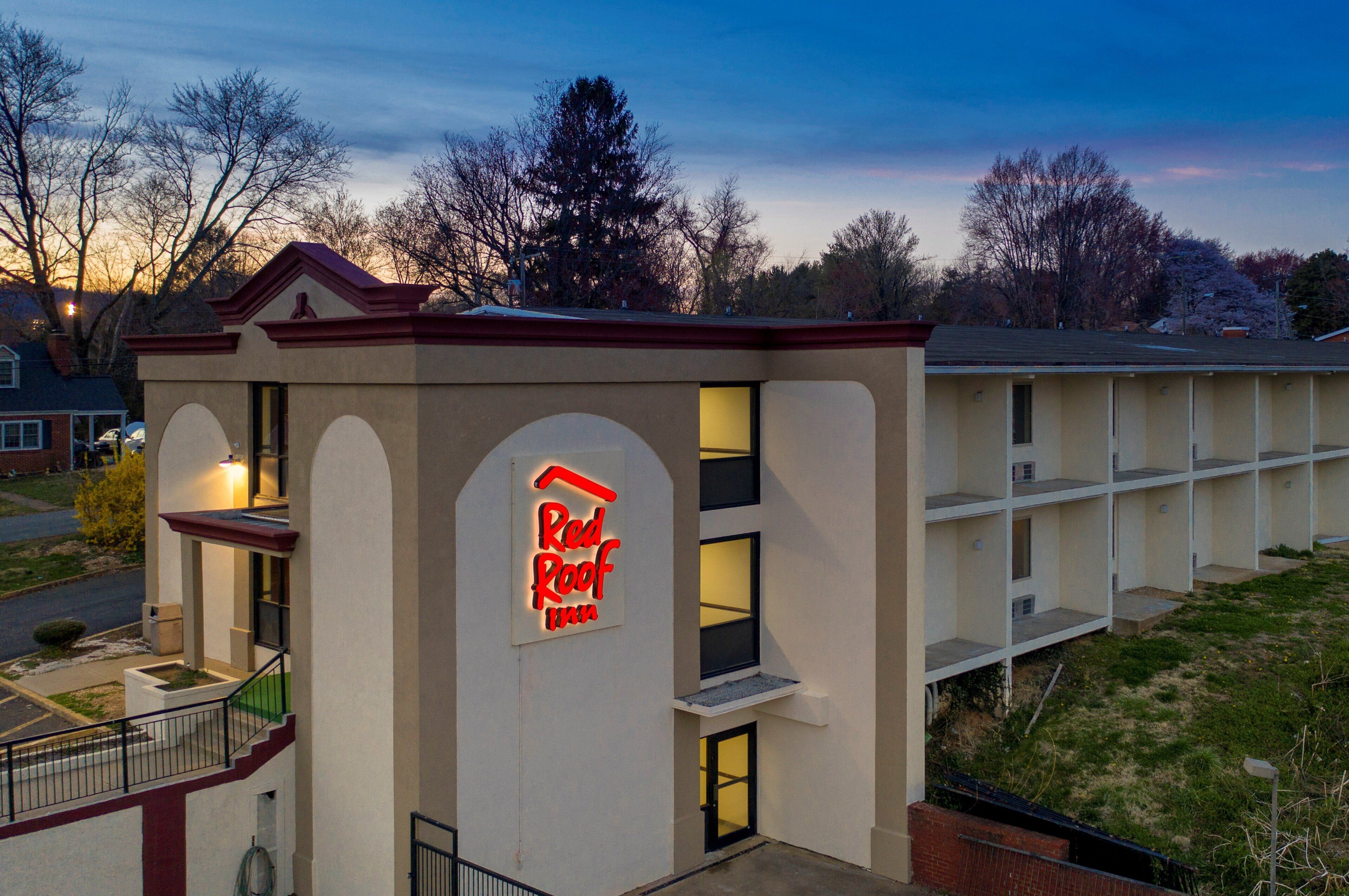 A Red Roof Inn with a prominent neon sign, a two-story building with a flat roof, and a parking lot in the foreground.