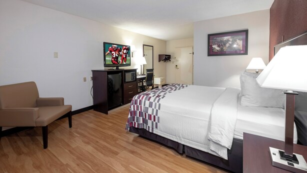 A hotel room with a bed, a desk with a computer, a chair, a TV, and a lamp.