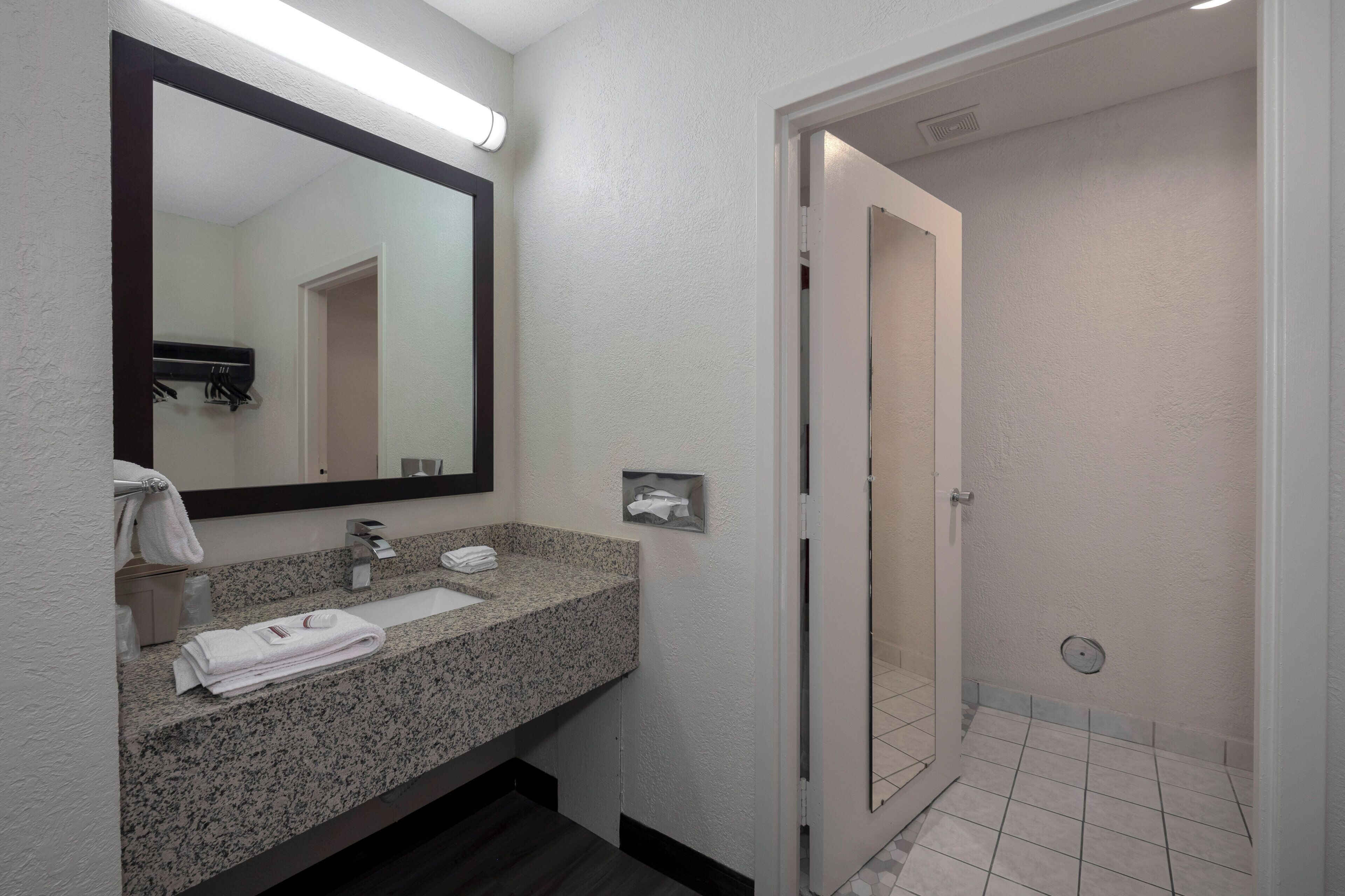 A bathroom with a granite countertop, a sink, a mirror, a towel rack, and a shower area.