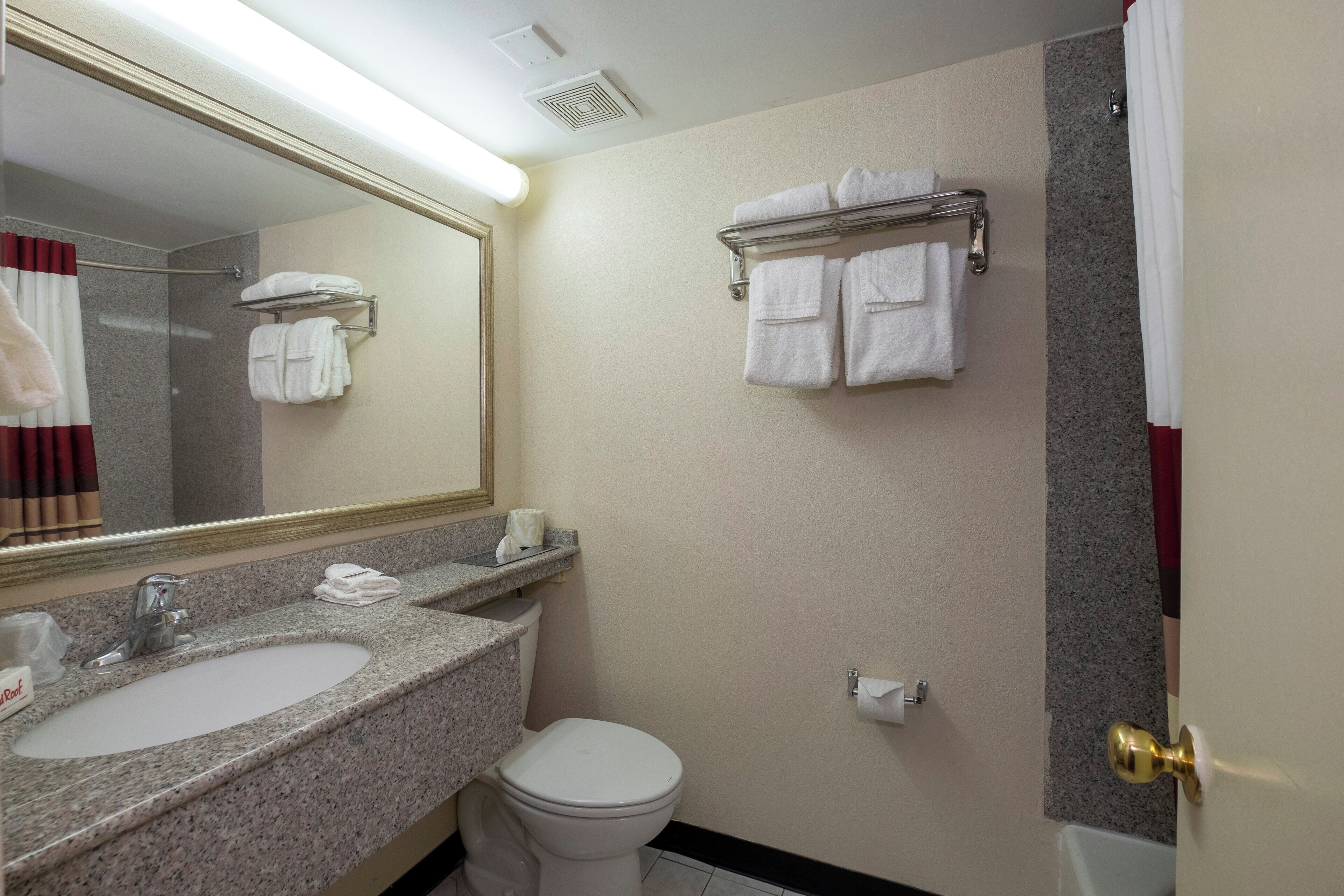 A bathroom with a granite countertop sink, a toilet, a towel rack with towels, a mirror, and a shower curtain.