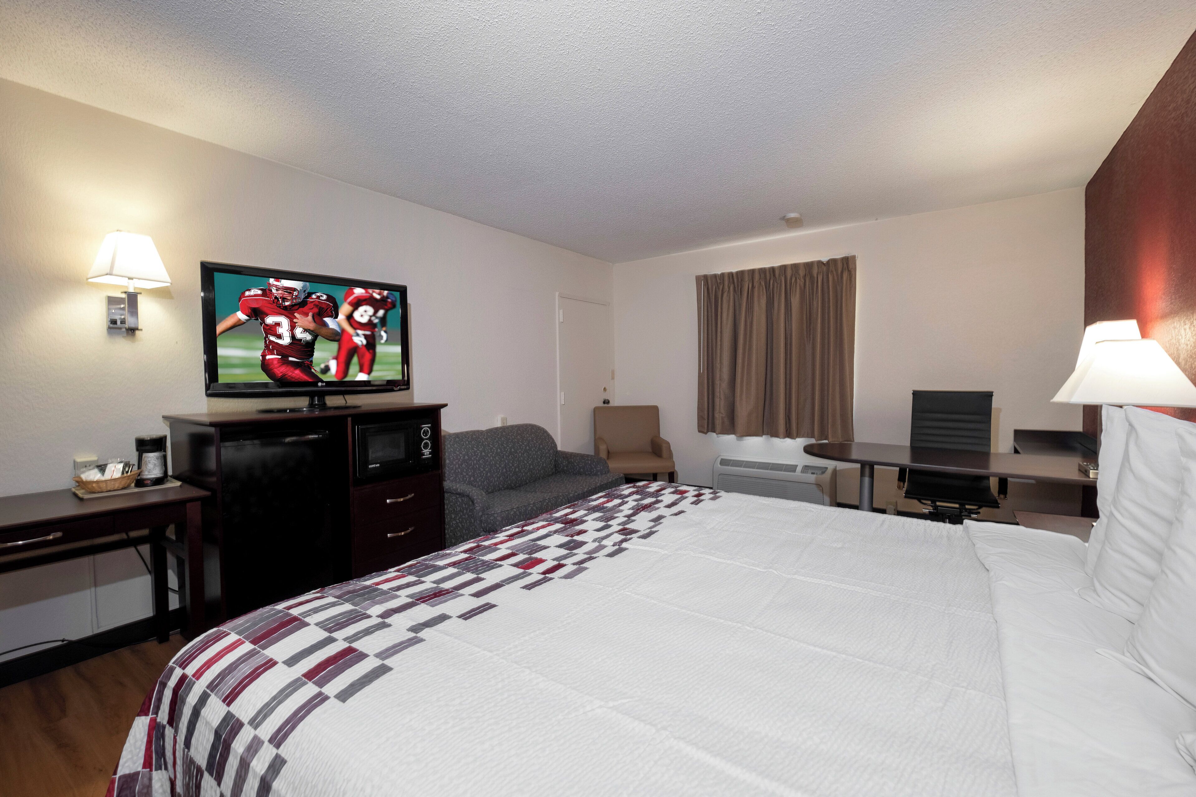 Habitación de hotel con cama, televisión, escritorio, silla y ventana con cortinas.