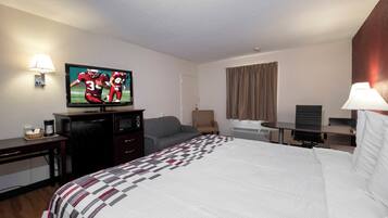Habitación de hotel con cama, televisión, escritorio, silla y ventana con cortinas.
