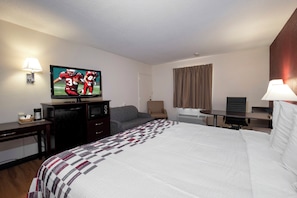 A hotel room with a bed, a television, a desk, a chair, and a window with curtains.