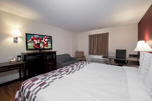 Quarto de hotel com cama, televisão, escrivaninha, cadeira e janela com cortinas.