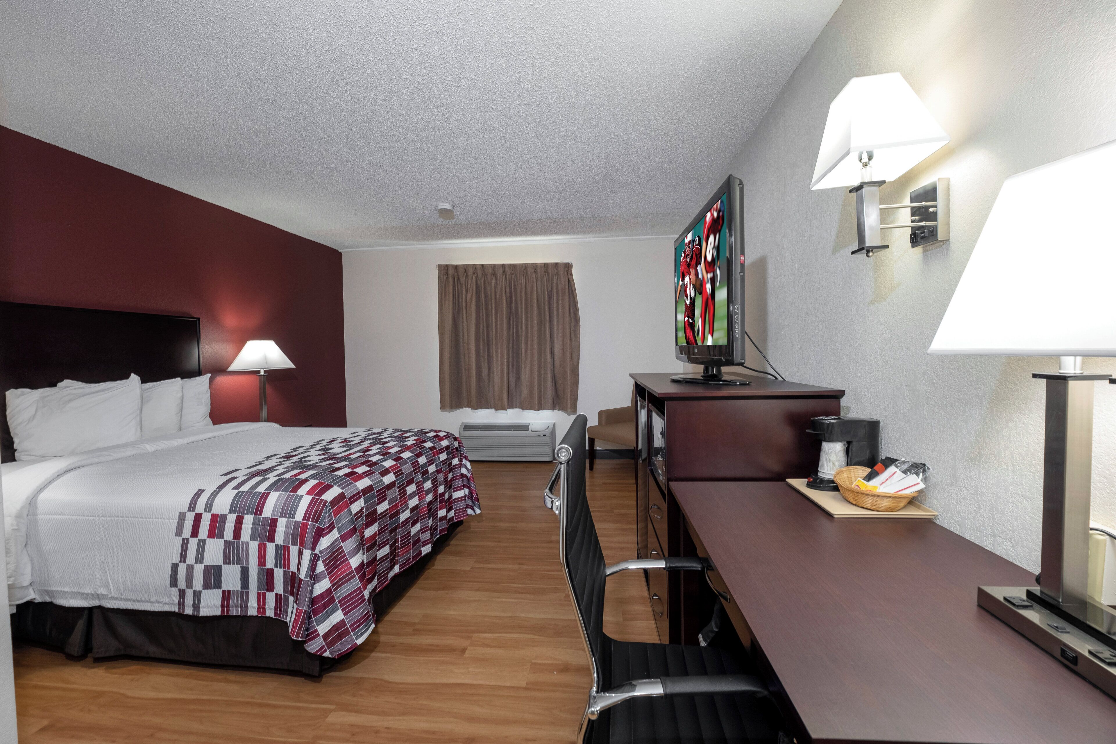 A hotel room with a bed, a desk, a chair, a television, and a lamp.
