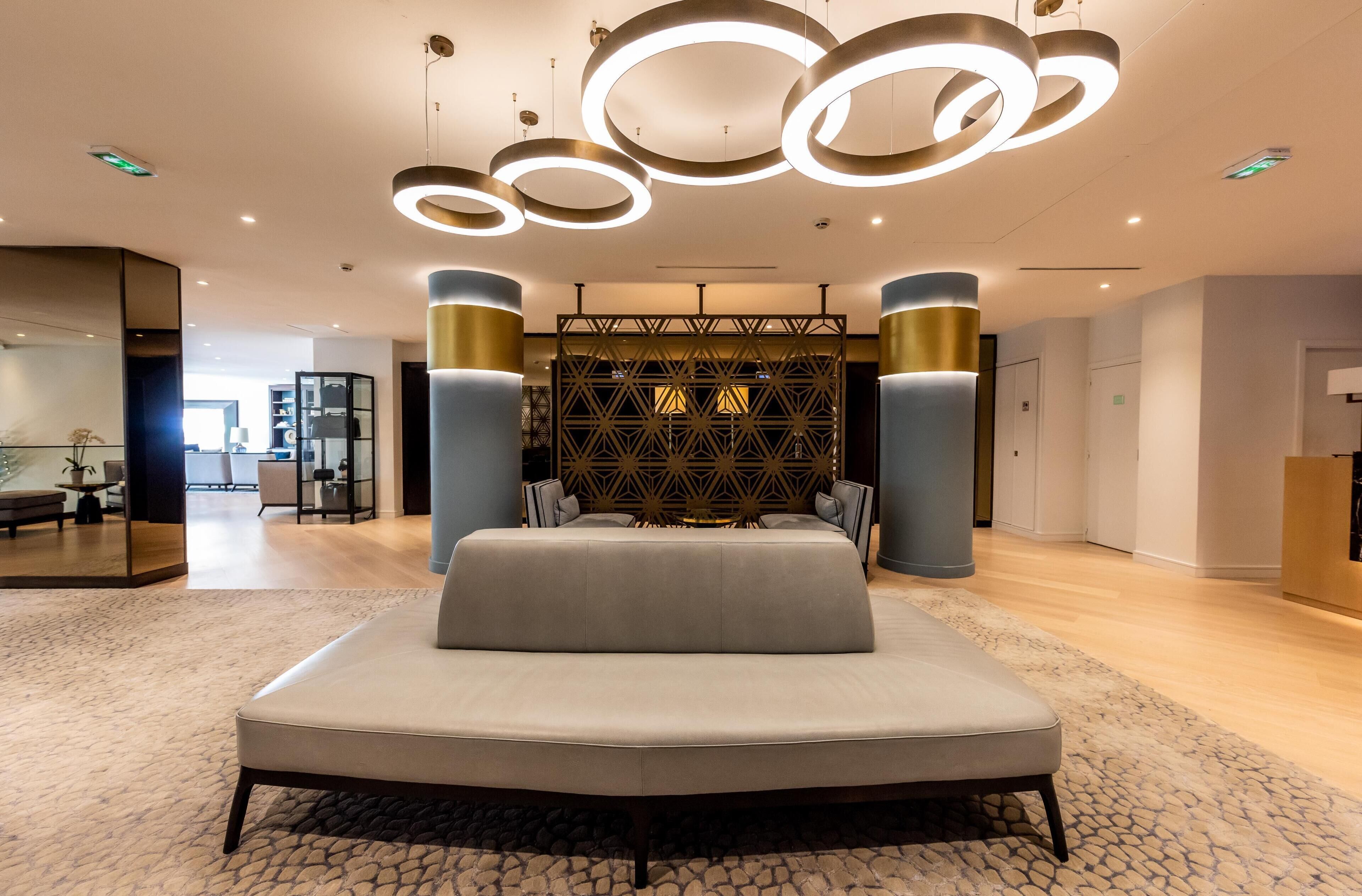 A modern hotel room with a large bed, a geometric patterned wall, and circular ceiling lights.