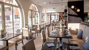 A spacious restaurant with high arched windows, modern furniture, and a well-lit interior. - Columbus Hotel Monte-Carlo, Curio Collection by Hilton (Monaco)