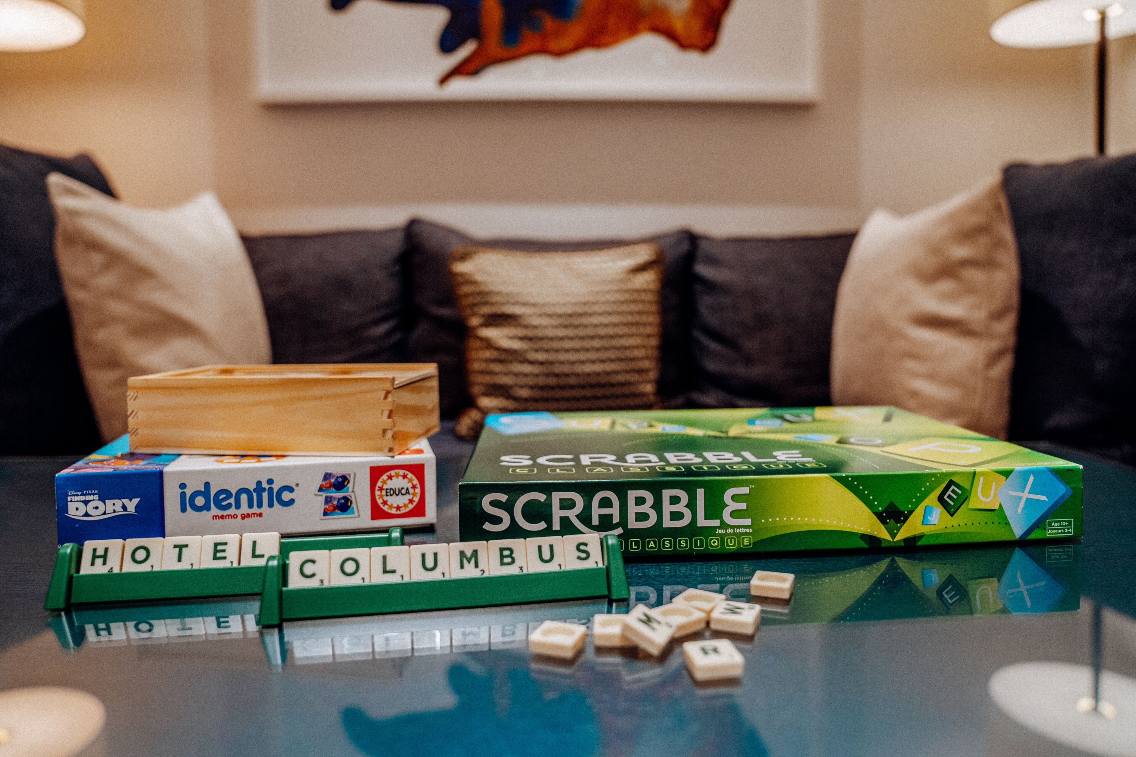 Un juego de Scrabble sobre una mesa de vidrio con fichas que deletrean "HOTEL" y "COLUMBUS" frente a un sofá con cojines.