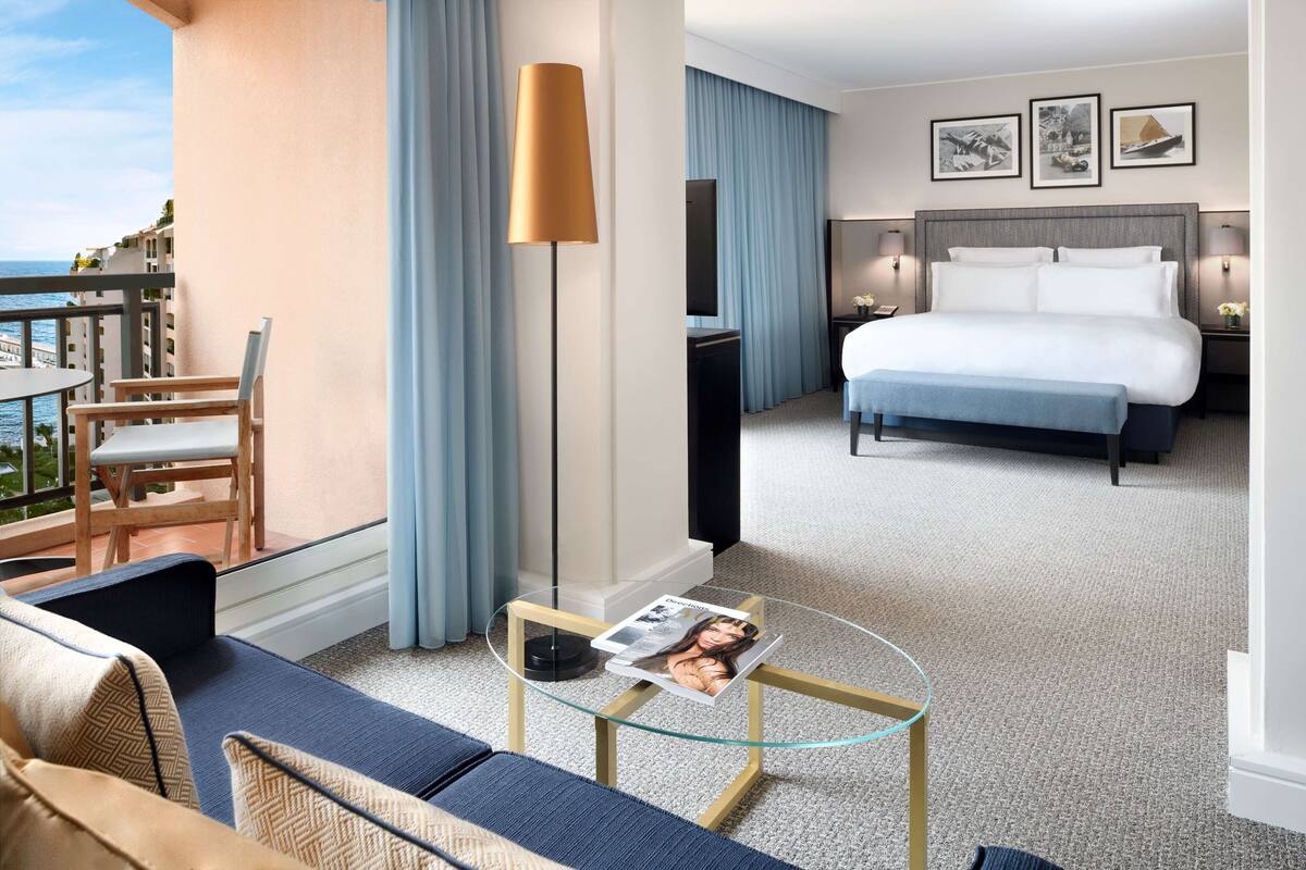 Ett hotellrum med en balkong, en säng, en soffa, ett soffbord i glas och en tv.