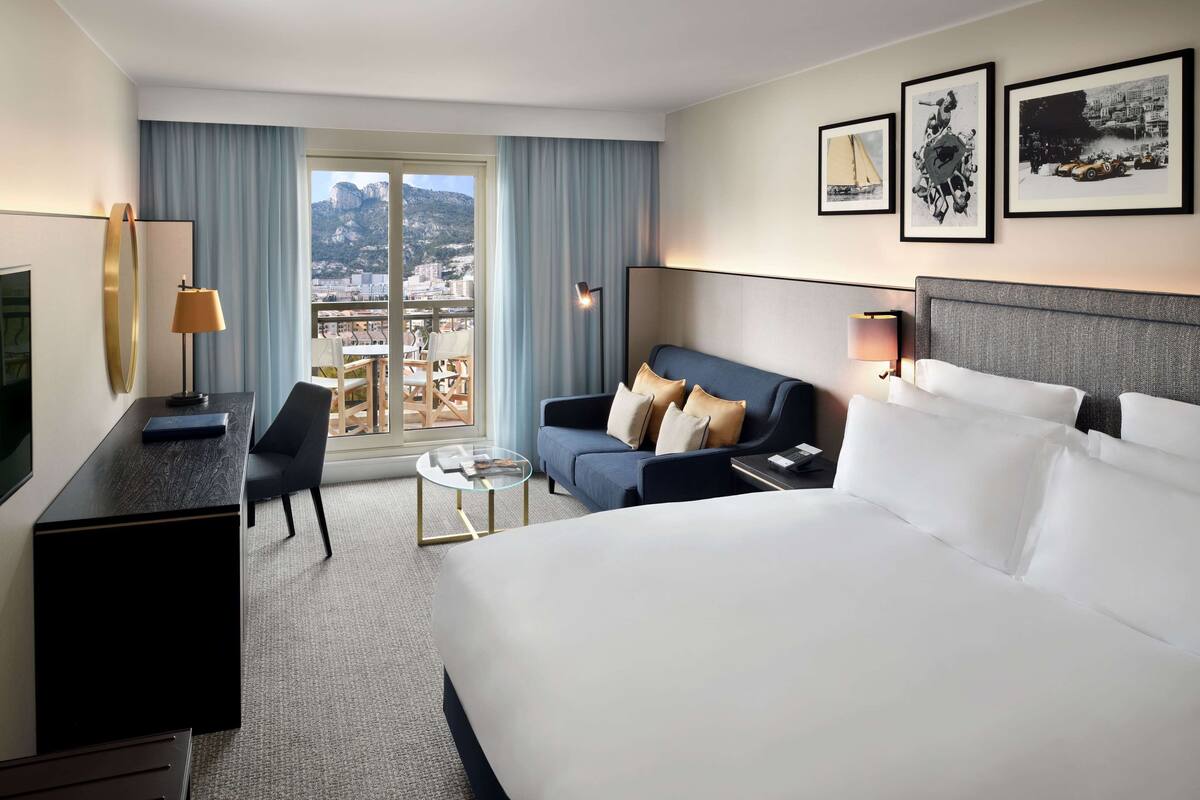 Ett hotellrum med en stor säng, en soffa, ett skrivbord och utsikt över staden.