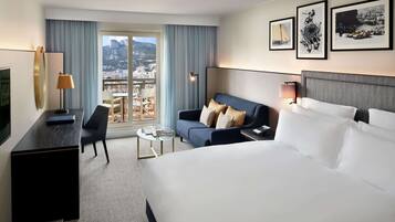 A hotel room with a large bed, a sofa, a desk, and a view of the city.