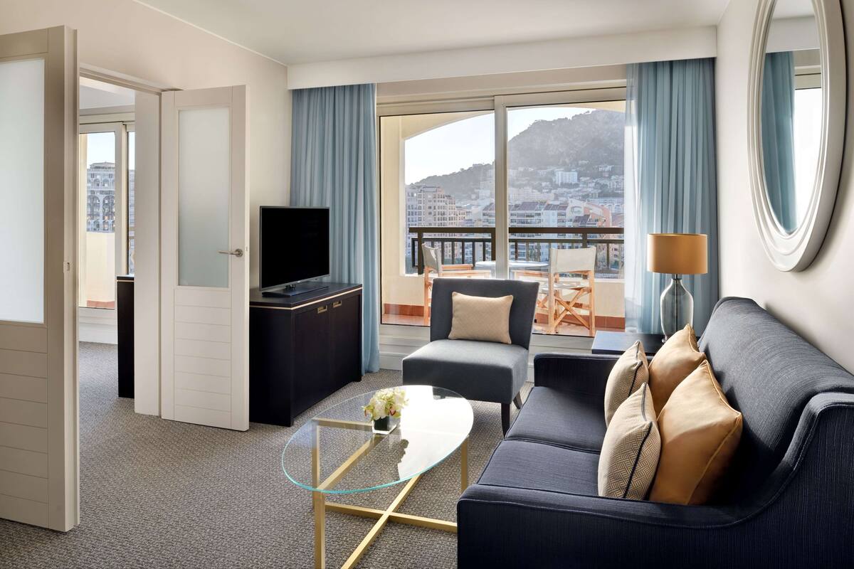 Ett modernt hotellrum med en balkong, en soffa, ett soffbord och en TV.