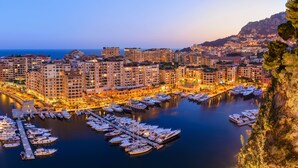 A marina with numerous boats docked, surrounded by multi-story buildings with balconies and a coastal backdrop. - Columbus Hotel Monte-Carlo, Curio Collection by Hilton (Monaco)