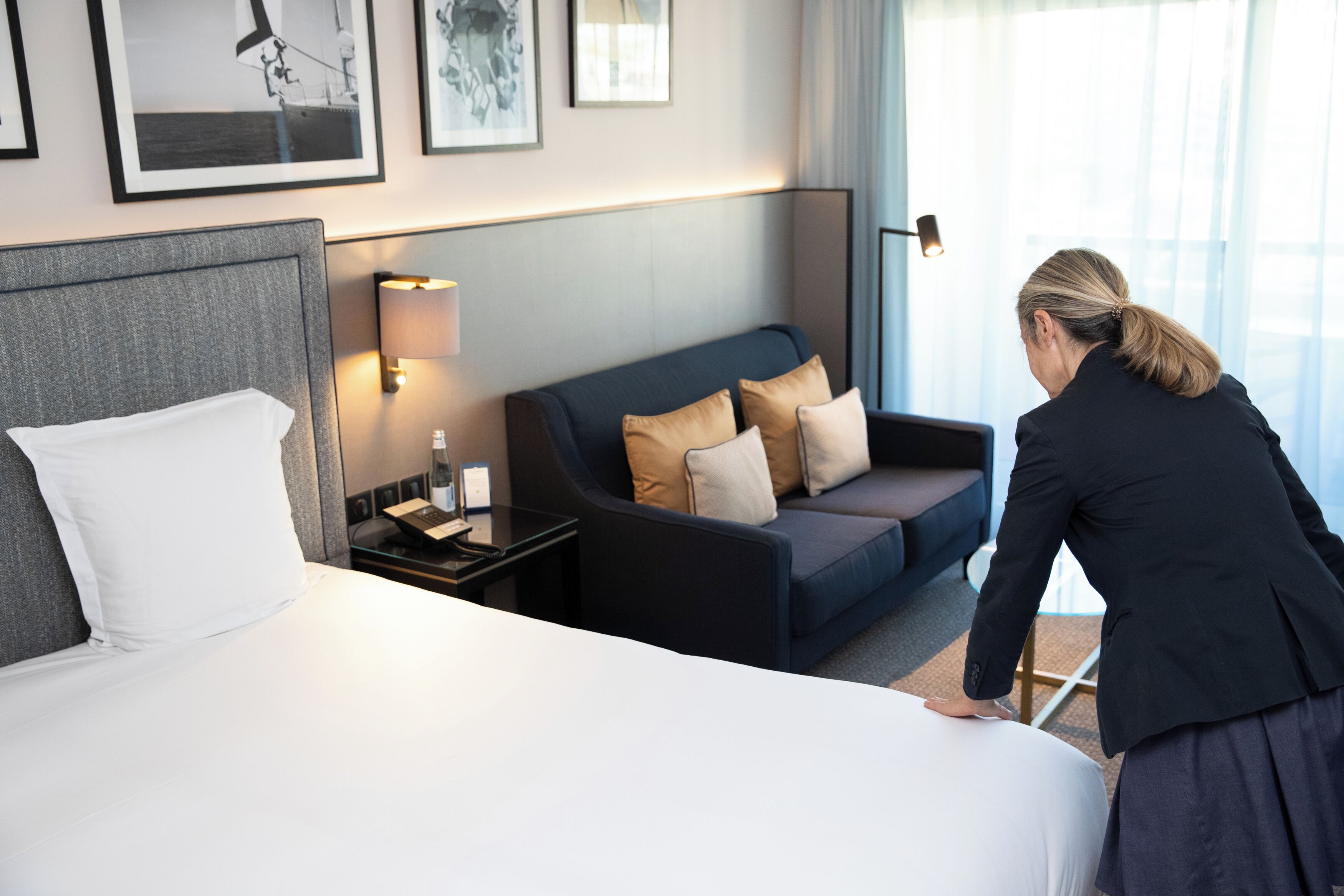 Una habitación de hotel con cama, sofá, mesita de noche con lámpara y cuadros en la pared.