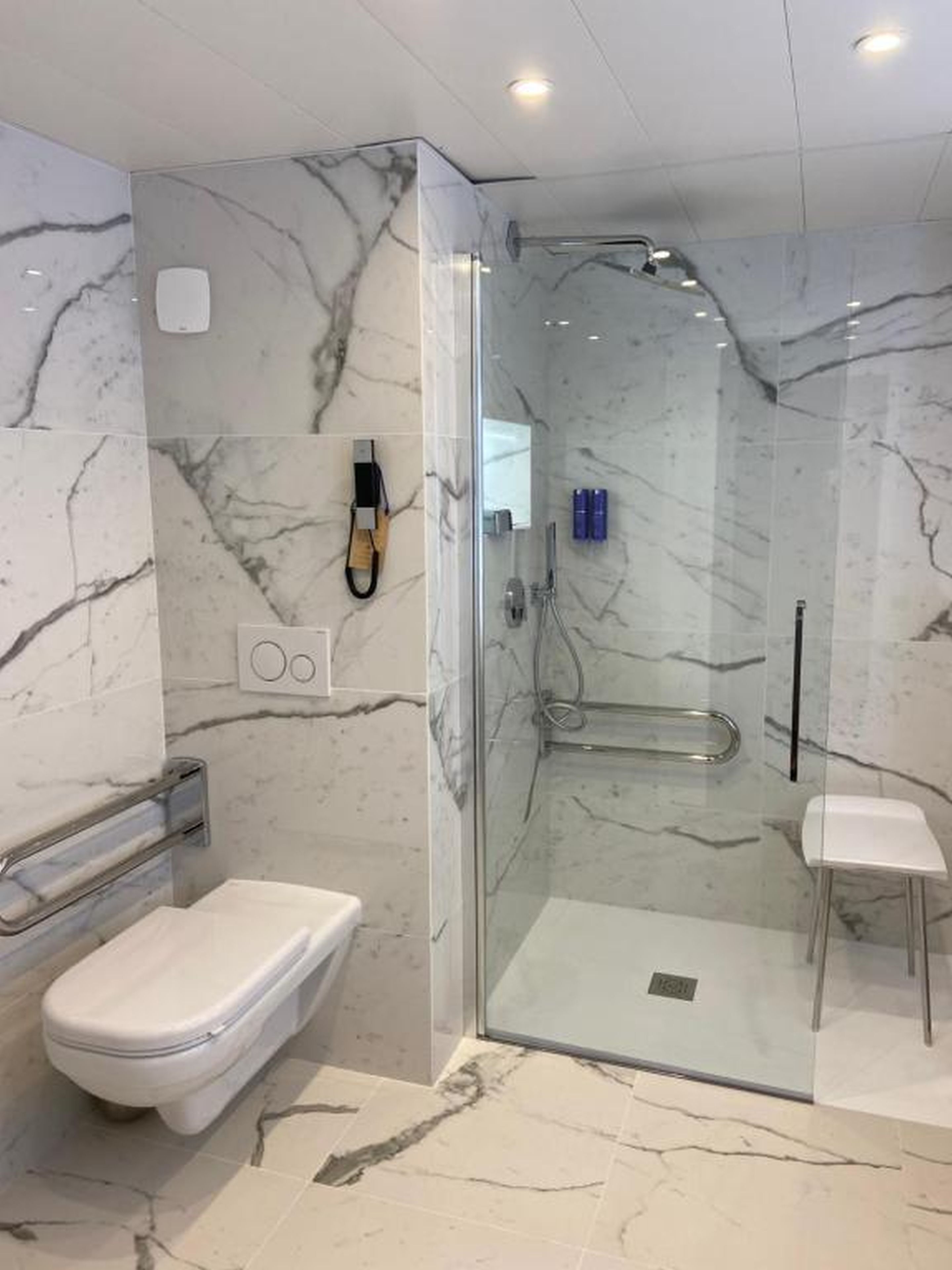Ein modernes Badezimmer mit einer Duschkabine, einer Toilette und einem kleinen Hocker.