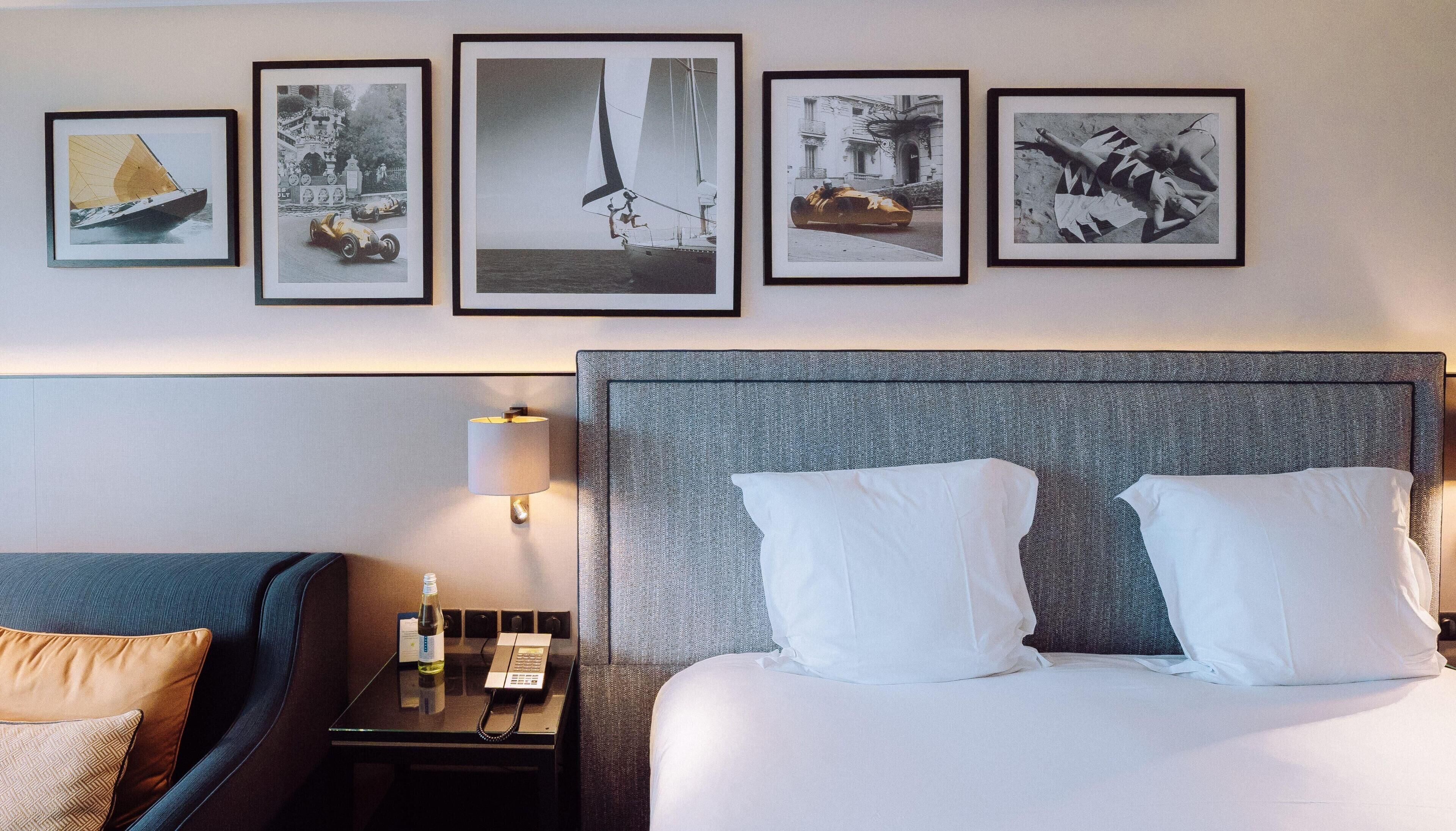 Una habitación de hotel con cama, mesita de noche, lámpara y un cuadro con marcos en la pared.