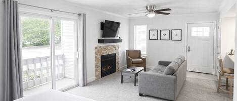 A hotel room with a bed, a fireplace, a sofa, a TV, and a ceiling fan.