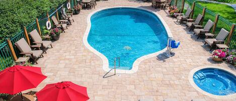 Una piscina con sillones de descanso y sombrillas, rodeada por un patio de ladrillo y vegetación.