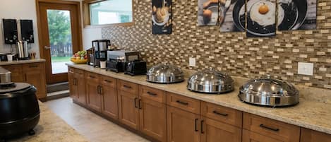 Una cocina con salpicadero de azulejos, armarios de madera, una encimera con equipamiento para servicio de alimentos y una ventana con vistas.