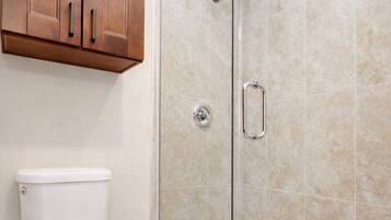 A bathroom with a toilet, a shower with a glass door, and wooden cabinets.