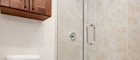 A bathroom with a toilet, a shower with a glass door, and wooden cabinets.
