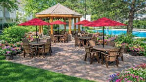 An outdoor patio with wooden tables and chairs, red umbrellas, and a gazebo.