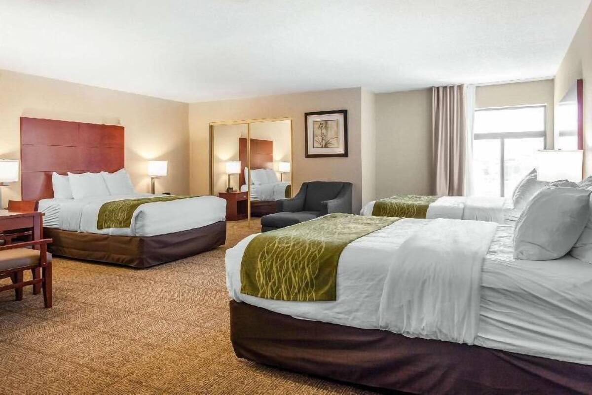 A hotel room with two beds, a desk, a chair, a mirror, and a window.