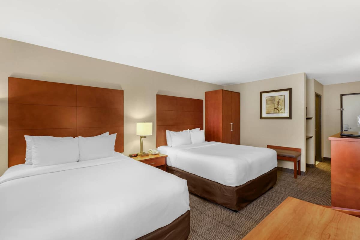 A hotel room with two beds, a desk, a chair, a lamp, and a painting on the wall.