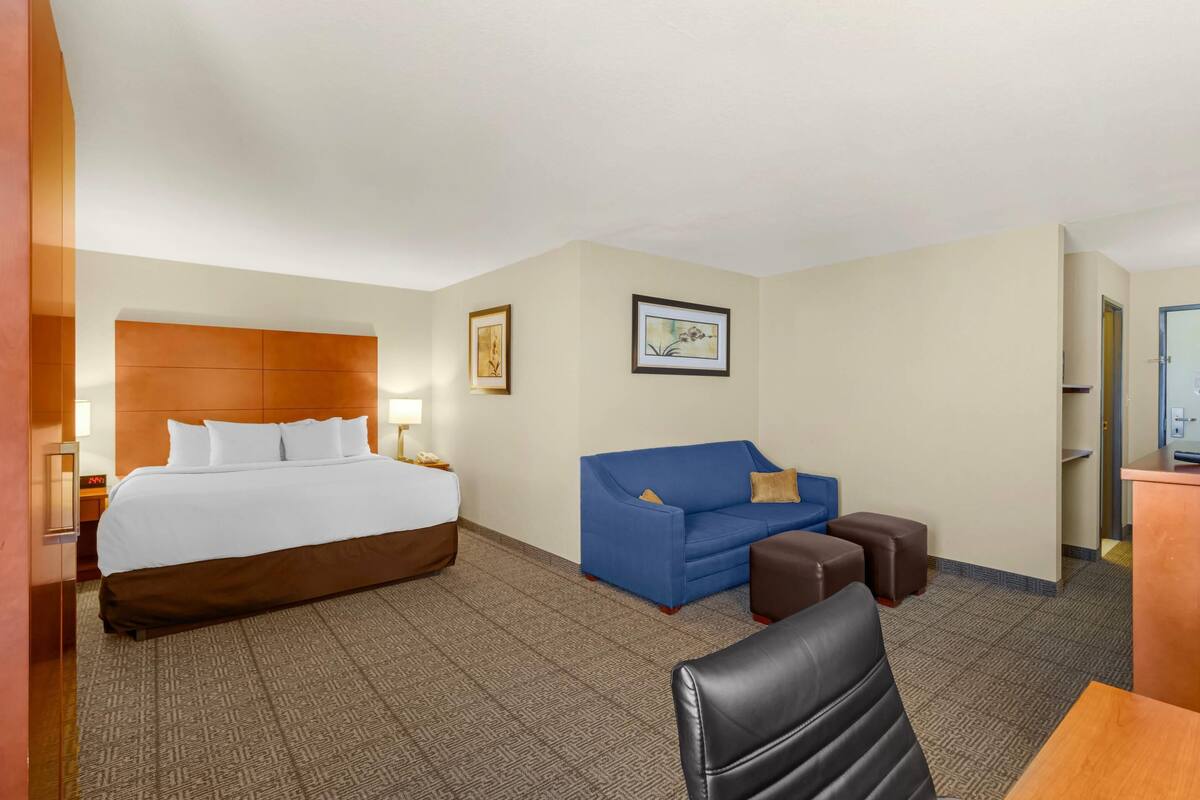 A hotel room with a large bed, a blue sofa, a wooden desk, and a black chair.
