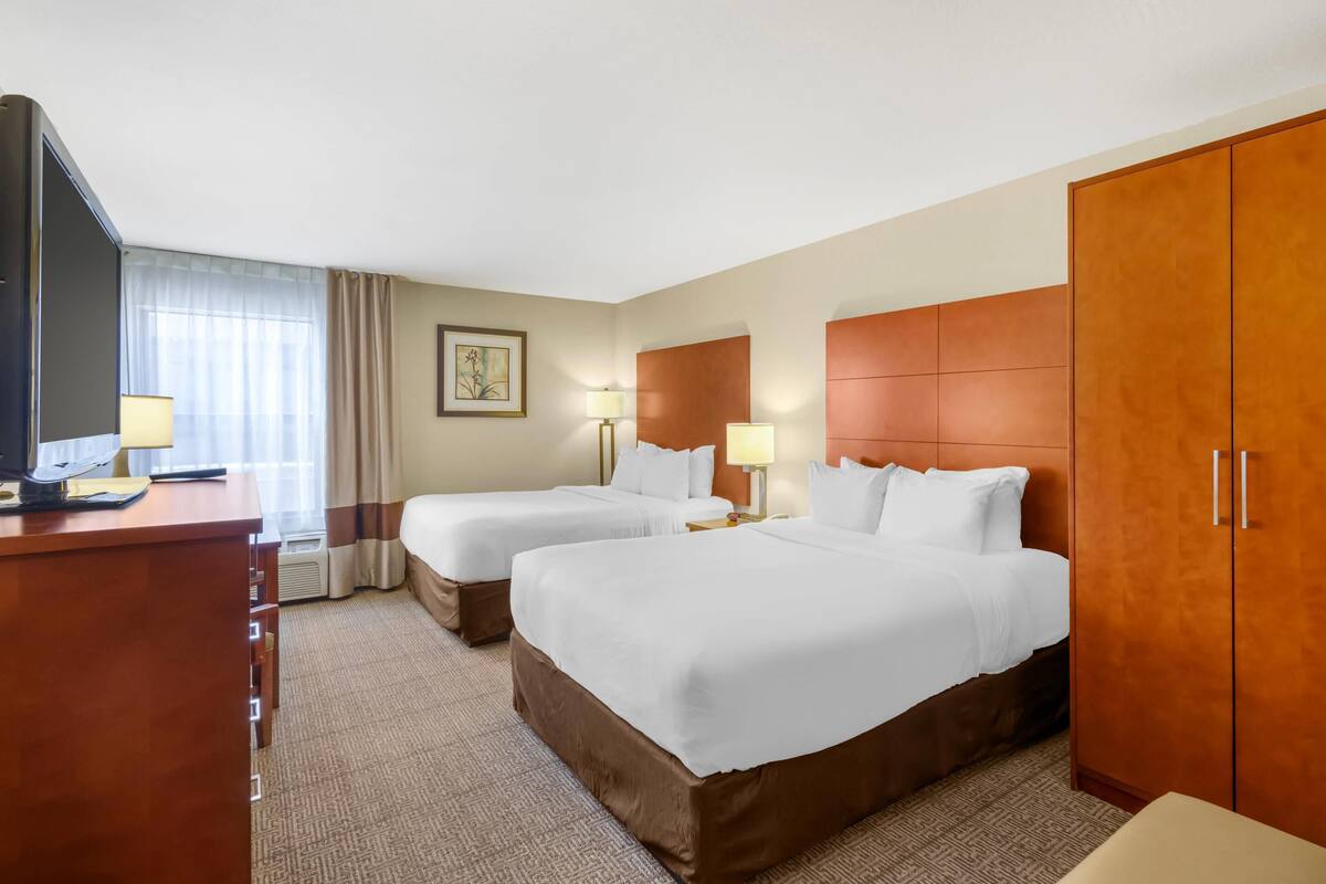 A hotel room with two beds, a desk, a TV, and a wardrobe.