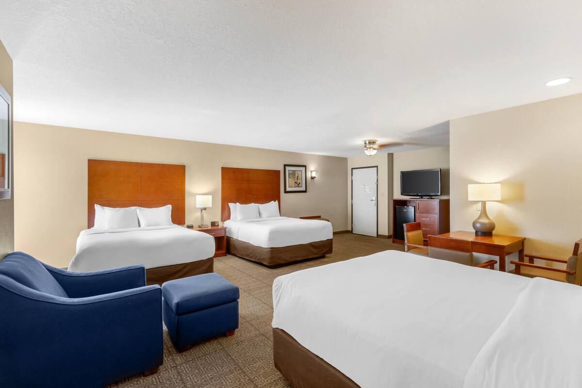 A hotel room with two beds, a desk, a chair, and a TV.
