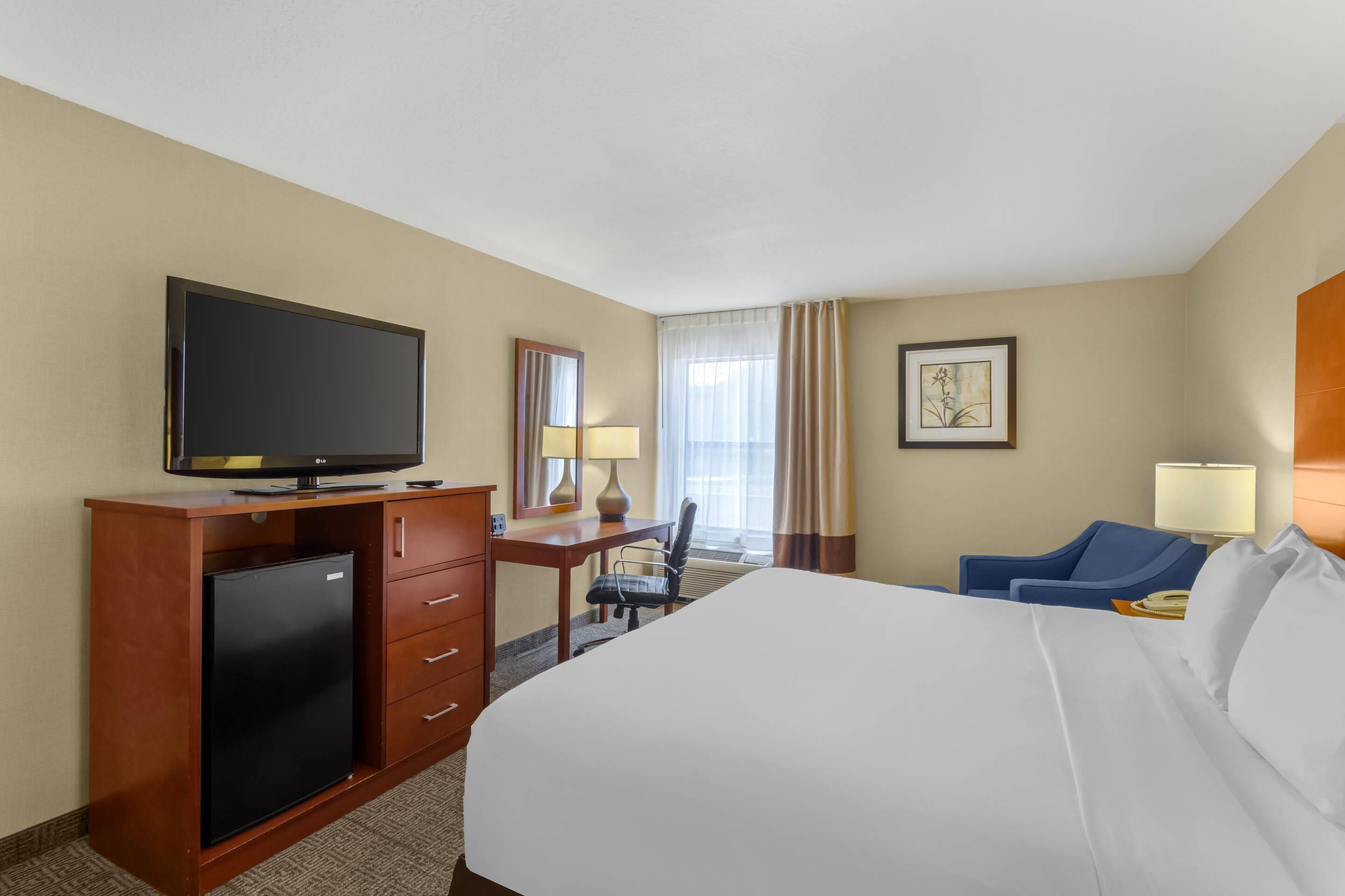 A hotel room with a bed, a desk with a computer, a television, and a chair.