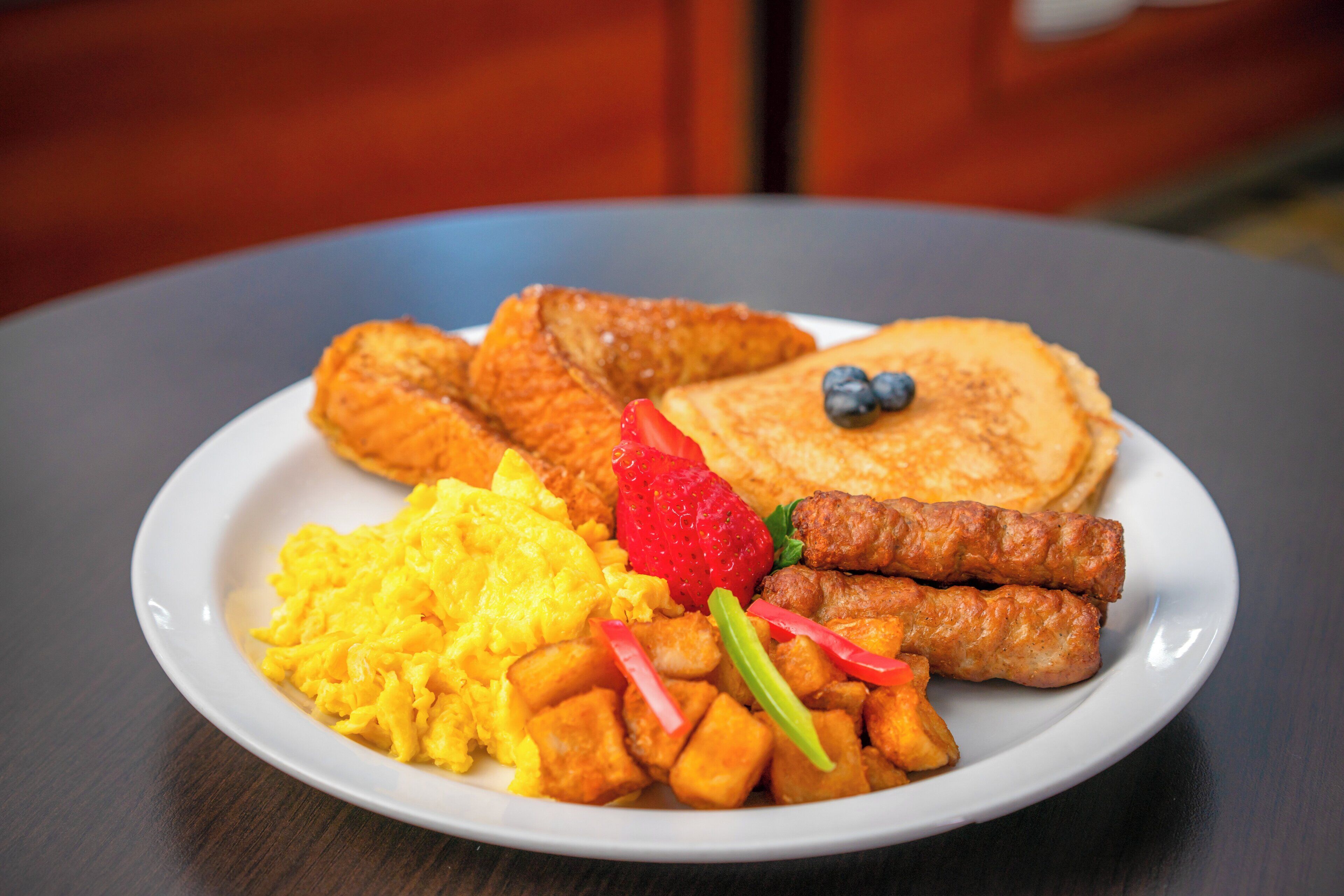 A plate of breakfast food including scrambled eggs, sausage, hash browns, and pancakes with fruit.