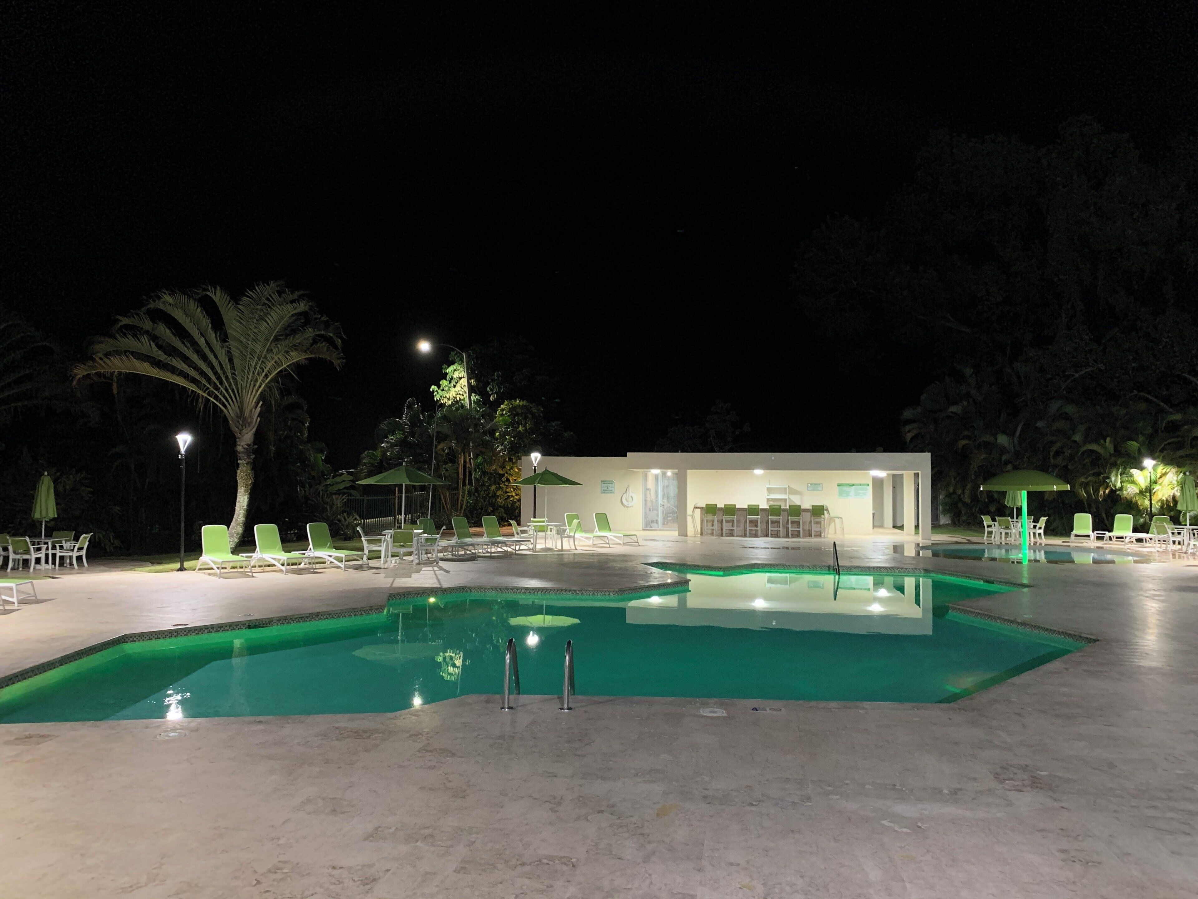 Ein Poolbereich bei Nacht mit Liegestühlen und einem Gebäude im Hintergrund.
