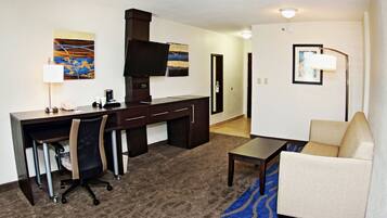 Habitación de hotel con escritorio, silla de oficina, sofá y alfombra estampada.