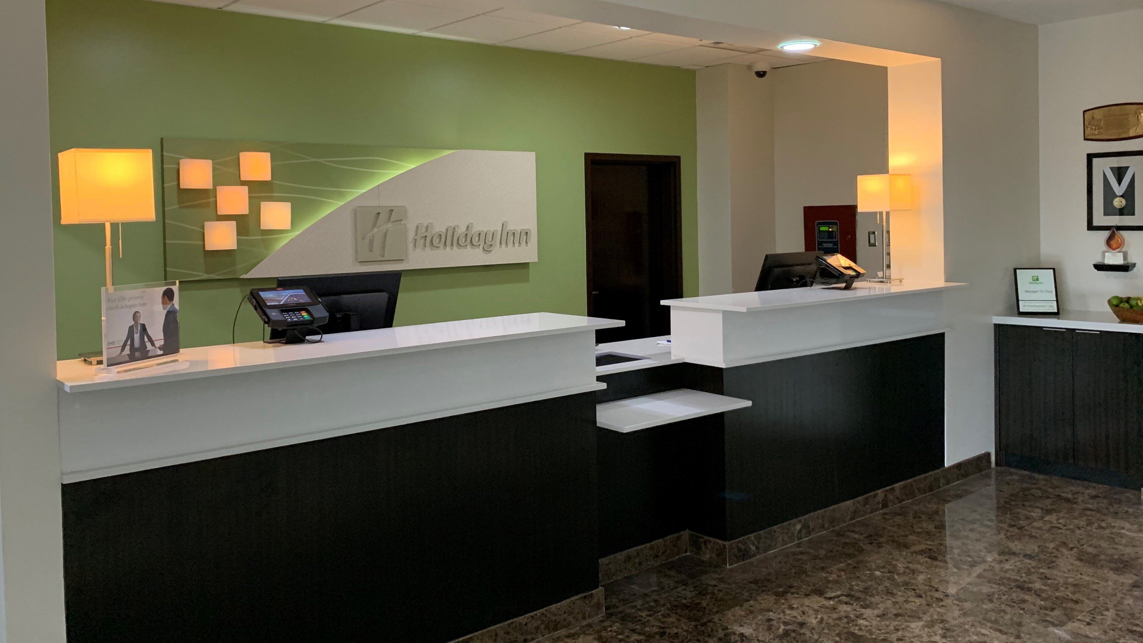 A hotel reception desk with a green wall, a digital screen, and a telephone.