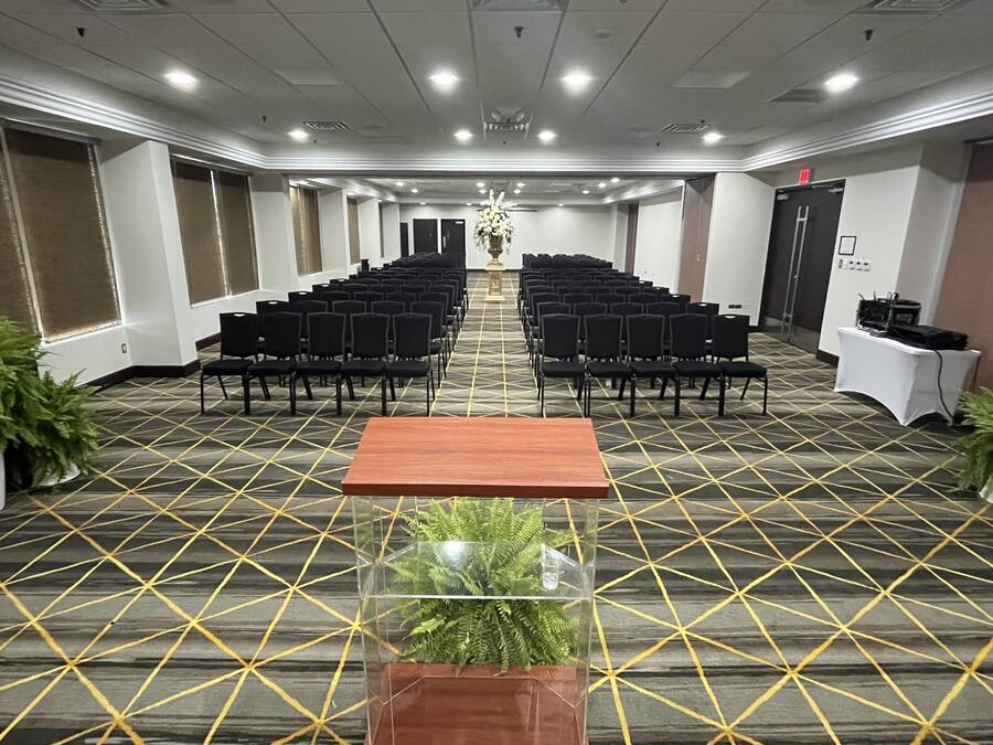 A conference room with rows of chairs, a podium, and potted plants.
