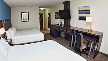 Ein Hotelzimmer mit zwei Betten, einem Schreibtisch, einem Sessel, einem Fernseher und einem Bild an der Wand.