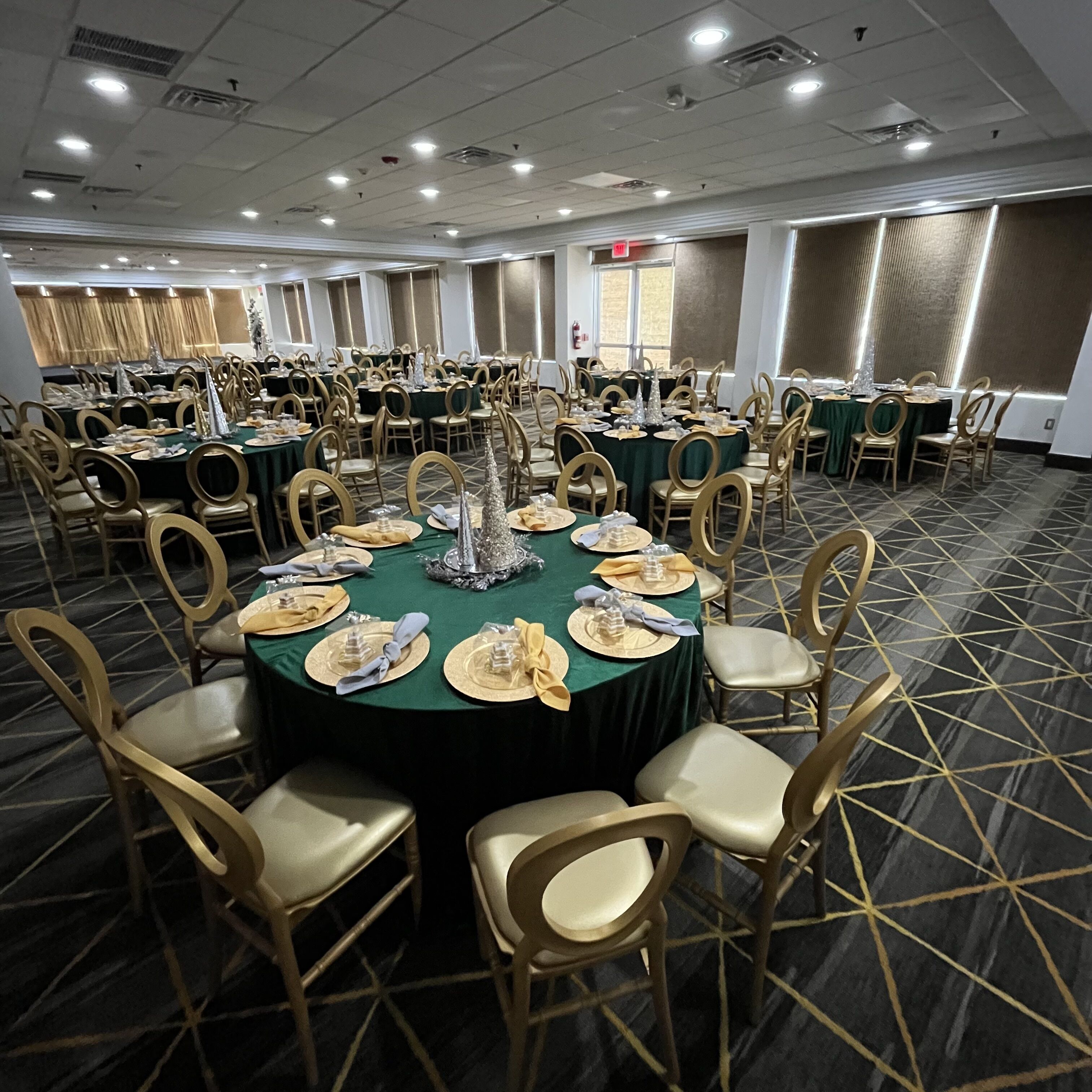 A banquet hall with round tables set for dining, each with gold chairs and green tablecloths.