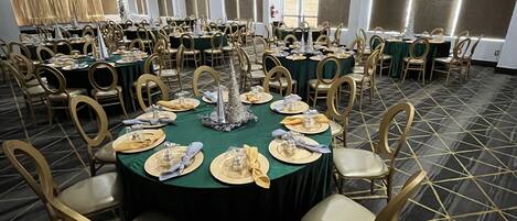 Un salón de banquetes con mesas redondas dispuestas para cenar, cada una con sillas doradas y manteles verdes.