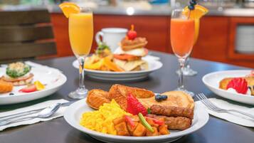 A breakfast setting with plates of scrambled eggs, toast, and pancakes, accompanied by orange juice and coffee.