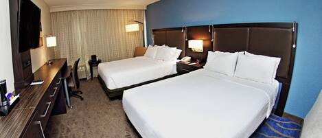 A hotel room with two beds, a desk, a chair, a TV, and a lamp.